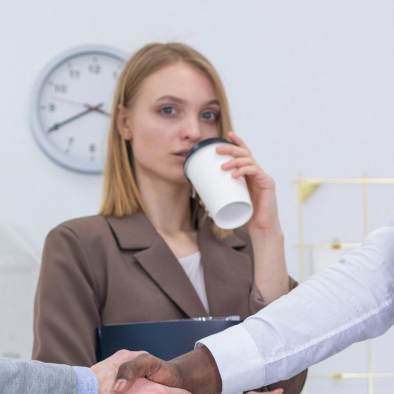 Femme buvant un café, observant une poignée de main entre deux hommes.