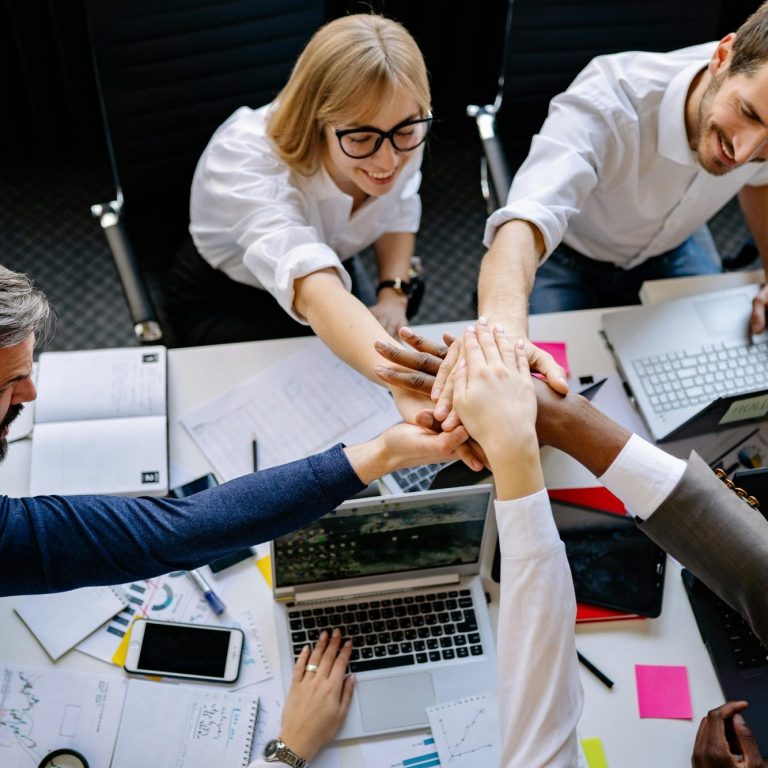 Groupe divers collaborant autour d'une table, unissant leurs mains en signe de coopération.