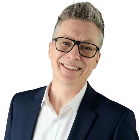 Homme souriant avec des lunettes, portant un costume et une chemise blanche.