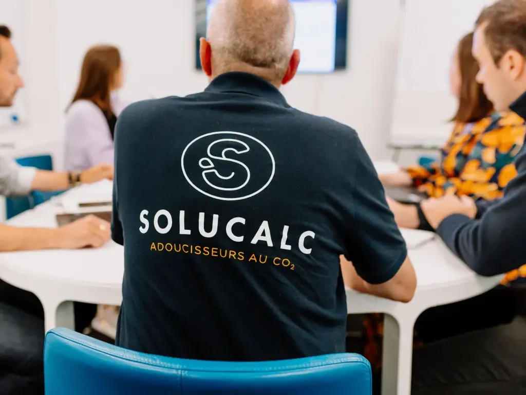 Groupe de personnes discutant autour d’une table, logo SoluCalc visible à l'arrière du tee shirt