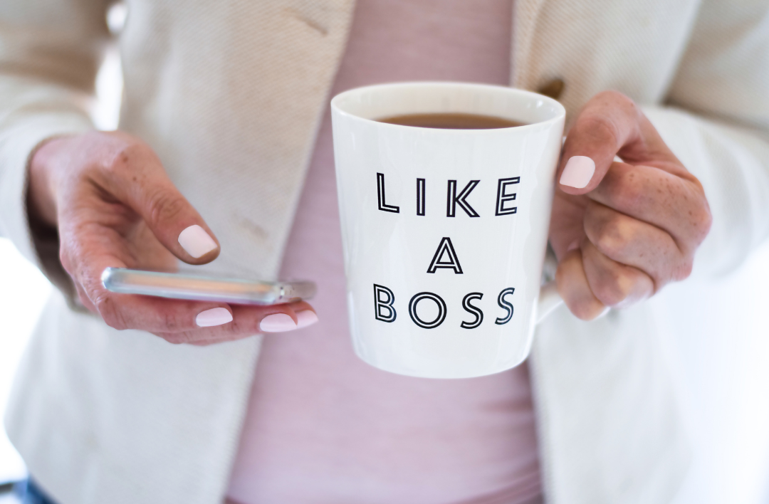 Tasse blanche avec l'inscription "LIKE A BOSS" et un smartphone dans l'autre main.