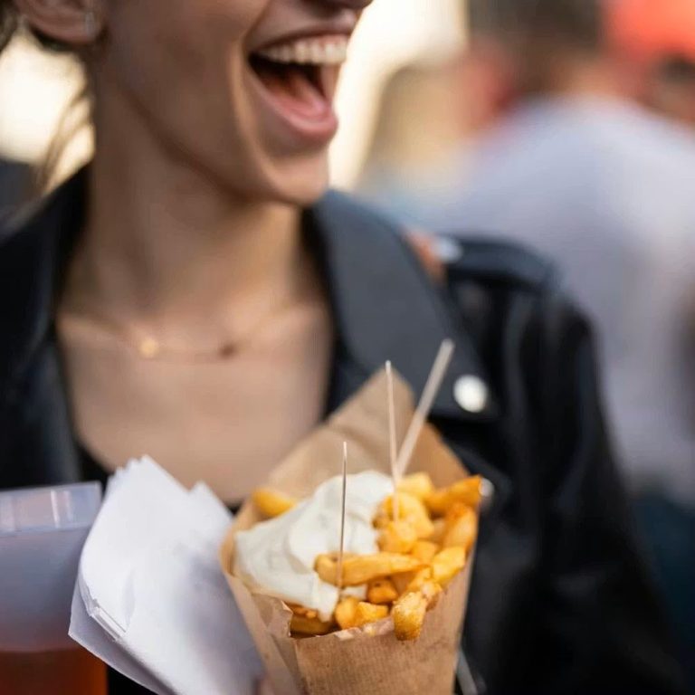 Femme souriante tenant des frites avec une sauce dans un cornet en papier.