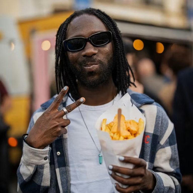Homme avec des lunettes de soleil tenant un cornet de frites, faisant un signe de paix.