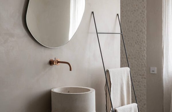 Vasque circulaire, robinet cuivré, miroir ovale et serviette suspendue sur un support.