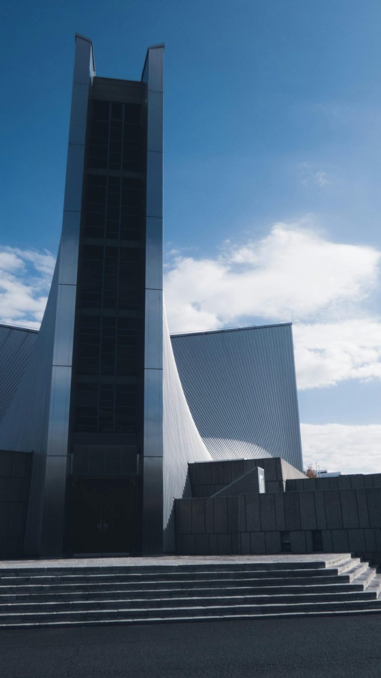 Édifice moderne avec une grande structure verticale et des lignes géométriques sous un ciel bleu.